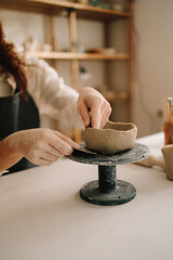 Poster - Craftswoman carefully molds a clay bowl on the potters wheel. Creating ceramic crockery in the workshop.