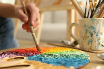 Wall Mural - Man with paintbrush mixing paints on palette at table indoors, selective focus