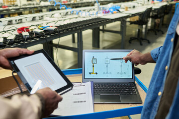 Leinwandbilder - Hand of male worker of factory pointing at laptop screen with schemes while explaining colleague with lamp how it works