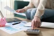 © New Africa - Budget. Woman with calculator, paperwork and laptop at wooden desk indoors, closeup