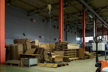 Aufkleber - Row of stacked cardboard sheets on pallets and packed boxes standing on the floor of spacious warehouse with equipment