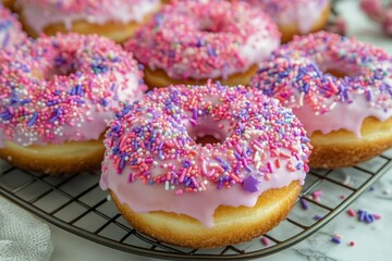 Wall Mural - Colorful pink glazed donuts with sprinkles on a cooling rack at a bakery