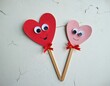 © miss irine - Two smiling hearts on sticks, kids craft. Red and pink hearts with googly eyes and bows. Children art project, handmade gift for Valentine day. Cute DIY decoration, fun paper toy.