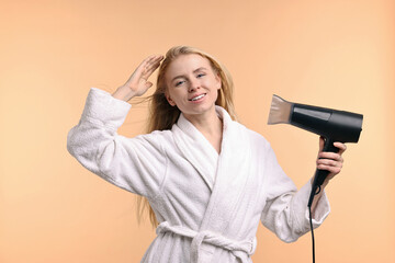 Wall Mural - Beautiful young woman drying her hair with hairdryer on beige background