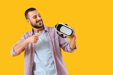 young man pointing at vr glasses on yellow background