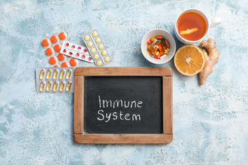 Wall Mural - Chalkboard with text IMMUNE SYSTEM, pills, cup of tea, orange and ginger root on color grunge background