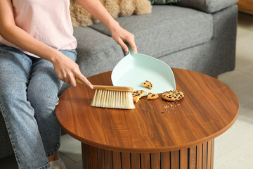 Poster - Young woman taking away cookie crumbs from table in living room. Closeup