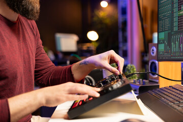 Fototapete - Composer artist twisting pre amp knobs and adjusting volume levels in home studio, mixing and mastering tunes for post production. Young singer recording and editing soundtracks.