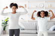 © Prostock-studio - Strong afro-american mother and teen daughter in sportswear showing their muscles while doing morning exercises together at home, athletic black family demonstrating biceps and smiling