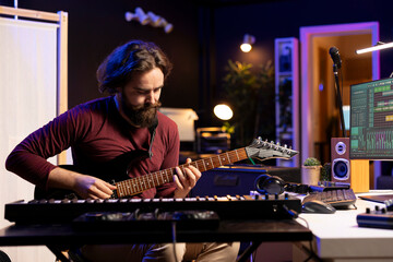 Leinwandbilder - Talented musician playing acoustic guitar while he records tunes on daw software for mixing and mastering session, home studio gear. Skilled artist recording his musical instrument tracks.