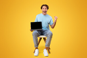 Wall Mural - Online Win. Vertical portrait of excited happy guy holding pc laptop with black blank screen, shaking clenched fist making winner gesture, screaming yes showing device with empty free space for mockup