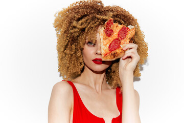 Stylish woman with curly hair holding pizza slice, vibrant red dress, playful expression on white background, representing fun and indulgence in healthy eating