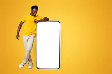 Wall Mural - Happy African American Guy Leaning On Big Smartphone With Empty White Screen, Cheerful Young Black Man Recommending New Mobile App, Promoting Online Offer Or Website, Beige Background, Mockup