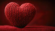 © Herdi - Close-up of a handcrafted red knitted heart on a red fabric surface against a dark red background.