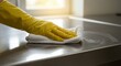 © IbragimovN - Hand with yellow glove cleaning kitchen counter with white cloth in sunlit room