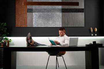 Informal atmosphere in the office, businessman threw his legs on the table and reads notes in the diary. An executive is working in the office. Feet on the office desk.