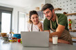 © NDABCREATIVITY - Young couple using laptop computer to take part in online culinary workshop, cooking together