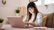 © JustFun - A Young Woman with Long Hair and Glasses Working on a Pink Laptop in a Comfortable Home Environment with Stylish Decor and Indoor Plants
