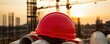 © PengAI - A red hard hat rests on pipes at a construction site, bathed in the warm glow of sunset with cranes in the background.