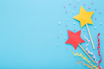 Wall Mural - Colorful star magic wands from application paper, confetti and small balls on light blue table background. Pastel color. Closeup. Empty place for text. Top down view.
