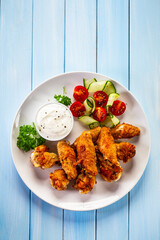 Wall Mural - Baked chicken wings with white dressing and fresh salad on wooden table	