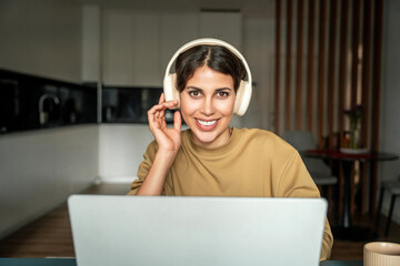 Canvas Print - Closeup portrait of young smiling latin freelance businesswoman in headphones using computer for remote business studying watching webinar. Student woman working on laptop pc at home looking at camera