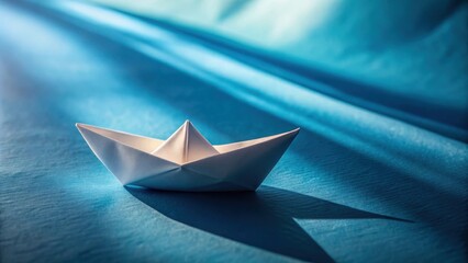 Aufkleber - A small paper boat floats on a tranquil blue surface, casting a long shadow in the sunlight.