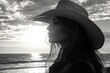 © ChaoticMind - Woman in cowboy hat gazes at sunset over ocean, silhouetted against dramatic clouds and reflective water
