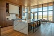 © BerkahStock - Modern kitchen with marble island, wood cabinets, and panoramic windows overlooking a scenic landscape.