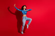 © deagreez - Joyful young woman dancing in bright outfit against red wall, showcasing contemporary fashion and lifestyle