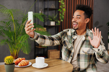 Canvas Print - Young fun man wear grey casual clothes doing selfie shot on mobile cell phone post photo on social network sitting alone at table in coffee shop cafe relax rest in restaurant during free time indoors.