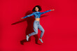 © deagreez - Stylish young woman in vibrant fashion jumping against red backdrop, exuding energy and joy.