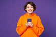 © ViDi Studio - Young surprised smiling happy Caucasian woman she wear orange hoody casual clothes hold in hand use mobile cell phone look camera isolated on plain purple background studio portrait Lifestyle concept