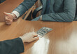 © alexey_arz - Hand moves dollar bills across an office table towards a man in a suit and tie sitting opposite. Give a bribe. Corruption