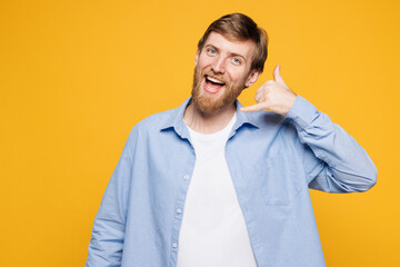 Wall Mural - Young smiling fun happy Caucasian man he wear blue shirt white t-shirt casual clothes doing phone gesture like says call me back isolated on plain yellow background studio portrait. Lifestyle concept.