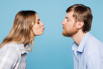 Wall Mural - Close up side profile view young couple two friends family man woman wear shirt casual clothes together going to kiss each other isolated on pastel plain light blue cyan background. Lifestyle concept.