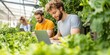 © Nuth - business startup with expansion. Two men working on laptops in a greenhouse surrounded by lush greenery.