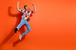 © deagreez - Young man in vibrant shirt jumping with joy against an orange backdrop, expressing freedom and happiness.