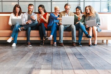 Wall Mural - group of diverse people sitting on a bench using laptops and tablets, engaged in technology and team