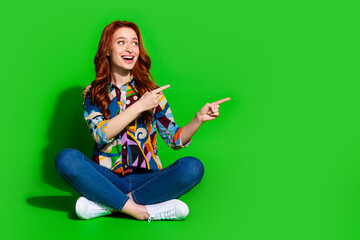 Wall Mural - Young red-haired woman pointing in excitement with a vibrant green background