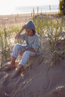 © saulich84 - A fashionable seven-year-old boy sit along a sandy beach by the sea in autumn in a sweater and hat at sunset.