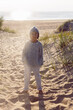 © saulich84 - A fashionable seven-year-old boy stay along a sandy beach by the sea in autumn in a sweater and hat at sunset.