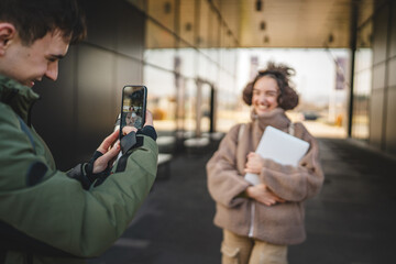 Wall Mural - young man take a photo on mobile phone of young woman outdoor