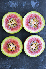 Wall Mural - Four slices of fig reveal a vibrant pink interior speckled with seeds, set against a dark, textured surface.