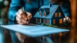 © MUMTAZ - Person signing a document beside a miniature house, representing home ownership and real estate