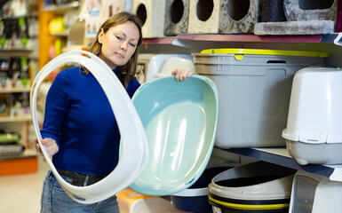 Young interested woman shopping for comfortable practical plastic litter tray for four-legged friend in pet shop