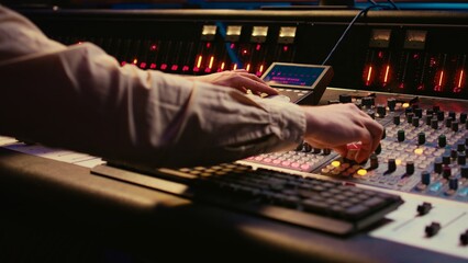 Fototapete - Sound designer working with sliders and switchers on control desk in professional music recording studio, editing and producing songs for a new album. Technician adjusting volume levels. Camera B.