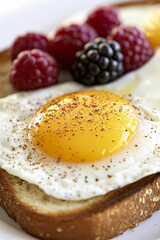 Canvas Print - Sunny-side-up egg on toast, garnished with vibrant raspberries and a single, dark blackberry.