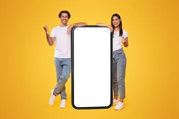 Wall Mural - yes. excited couple leaning on big smartphone with empty white screen shaking clenched fists, cheerf