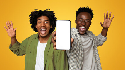 Wall Mural - Great App. Two Excited Black Guys Demonstrating Smartphone With Blank White Screen At Camera, Cheerful Young African American Friends Showing Free Copy Space For Your Ad Or Design, Mockup